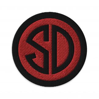 A circular embroidered patch with "SD" in black font on a red background