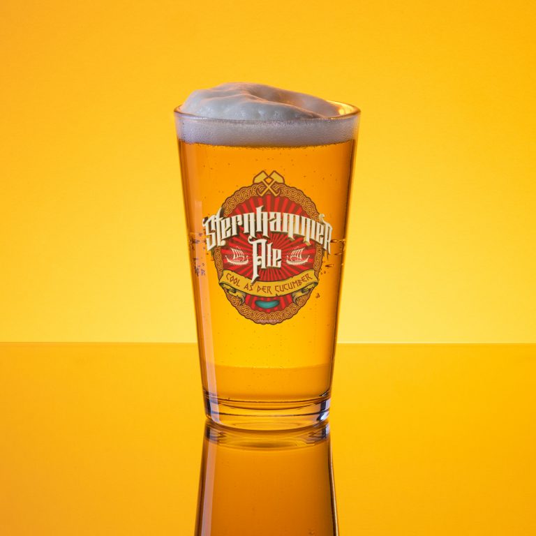 Amber lit image of a full foamy pint glass with a beer label embalm in the centre, the beer is called 'Sternhammer Ale' with a banner reading 'COOL AS DER CUCUMBER' underneath